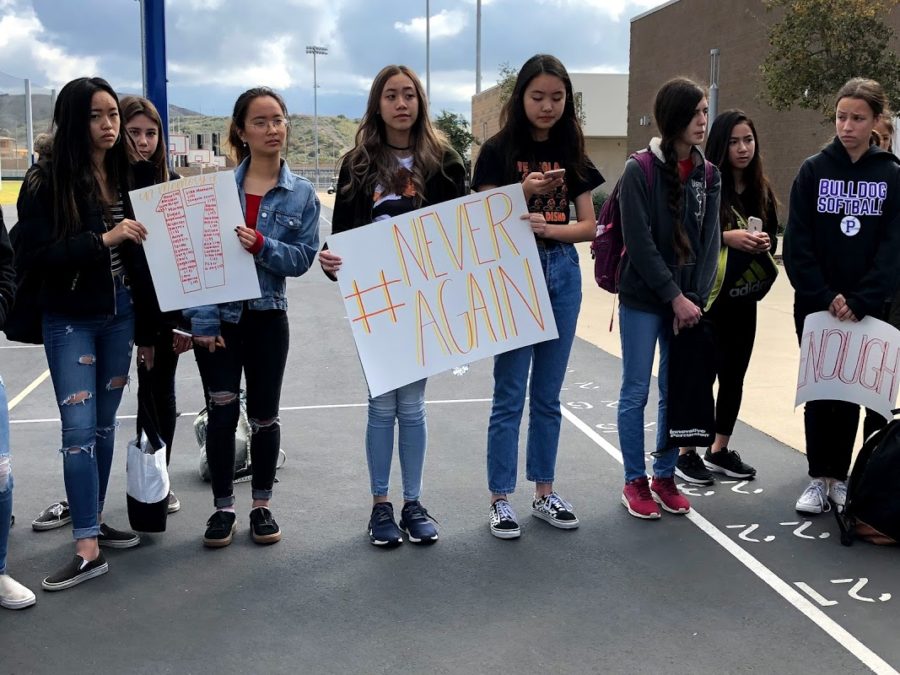Freshman Kelthie Truong holds a sign that says “#NeverAgain,” while freshman Kristen Ok keeps track of the 17 minutes as she reads off the names of those killed in the Florida shooting.