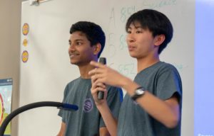Junior Aditya Sasanur and sophomore Ethan Hung introduce the four stations planned for the event, including Math Bingo, Non-Newtonian Fluids, Aluminum Foil Boats and Artistic Points of Interest. 