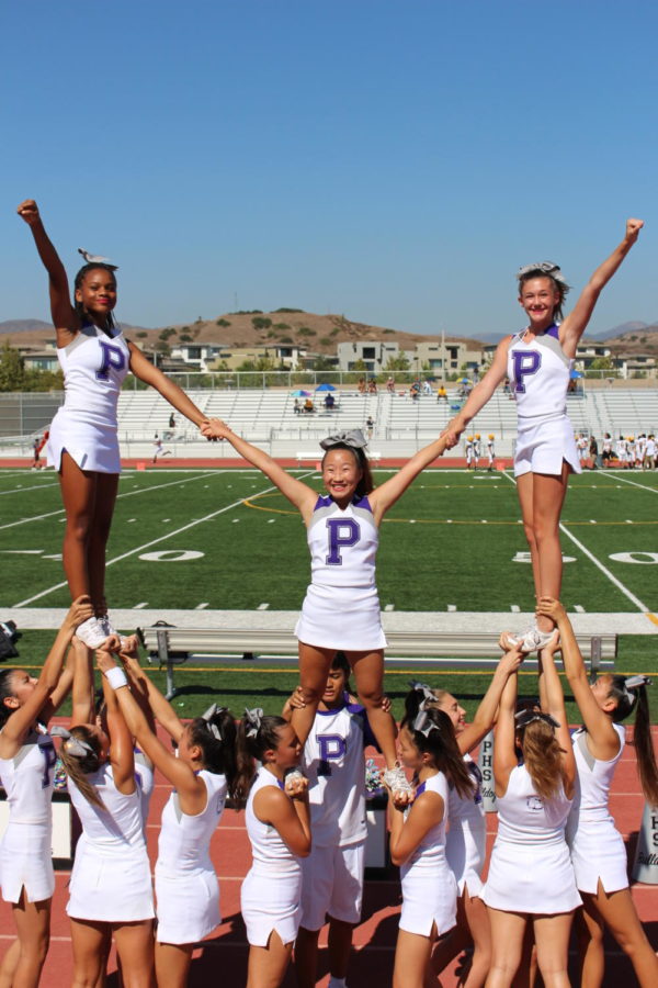 Freshmen side flyers Demetris Owens and Katelyn Toulmin stands next to sophomore center flyer Hailey Kim, in a stunt at a junior varsity football match against Laguna Hills High. 