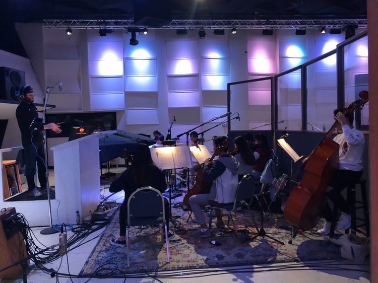Music teacher Desmond Stevens conducts the members of the orchestra as they record in the studio. In studio recordings, the musicians have to both follow the conductor and listen in the headphones for the metronome and cues.