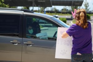 Education specialist Desiree Shaffer waves a “Go Bulldogs” sign to incoming cars of students and family members, who show their appreciation even behind windows and masks. From a safe distance, Shaffer stops to check in and chat with the families before sending them down the line of other cheerful staff members.
