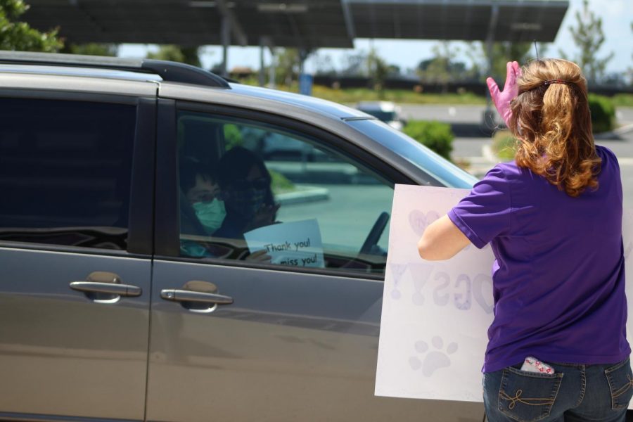 Education specialist Desiree Shaffer waves a “Go Bulldogs” sign to incoming cars of students and family members, who show their appreciation even behind windows and masks. From a safe distance, Shaffer stops to check in and chat with the families before sending them down the line of other cheerful staff members.
