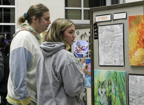 Junior Madison Curran shows her brother, Owen Curran, the displayed artwork. She was one of many visual arts students showing the art portfolios to her family. “I get to see that joy from students, like how excited they are to have their work showcased, to tell me what things they overheard and to get to see their vision for Night of Arts come to life,” visual arts teacher Kearci Thompson said.
