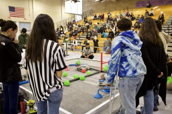 Student host and junior Audrey Kim serves as a referee for a qualification match. A triball, a green, blue or red pyramid-shaped object, scored in a goal is worth five points, and a triball scored in an offensive zone is worth two points. 