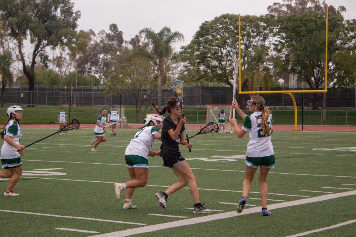 Attacker and sophomore Olivia Ganes scoops the ball and cradles it through two Vaquero players. Ganes was able to play more aggressively during this game, according to head girls’ lacrosse coach Julie Primero. “Olivia scoring three goals was crazy,” said utility player and sophomore Claire Hsin. “Im super proud of her for that.”