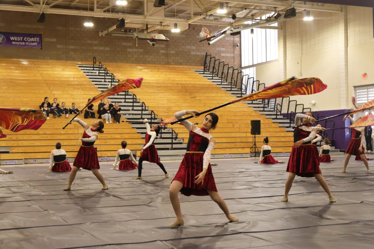 Color guard member and freshman Leia Speir performs during the flag feature, a piece of the show in which flag line members twirl their flags and dance in synchronization. Speir said that prior to each competition, the team has to go through a long process of hair, makeup and final practices.