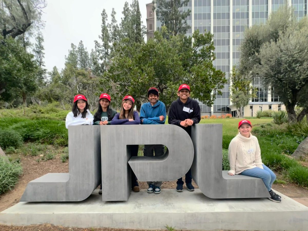 Team member and sophomore Melody Bao, alternate and junior Sandy Shanmuga-Nathan, co-captain and junior Kayley Winata, co-captain and junior Suhrith Muvvala, team member and junior Rishabh Garg and advisor and physics teacher Leanne Jimenez pose with the JPL sign at NASA’s Jet Propulsion Lab (JPL) after the competition. “[Science Bowl] is a really fun way to apply knowledge because you don’t get game-show style application of knowledge in school,” Muvvala said. “So it’s, one, for the fun, and, two, because I already have to study for Science Olympiad or Biology Olympiad.”