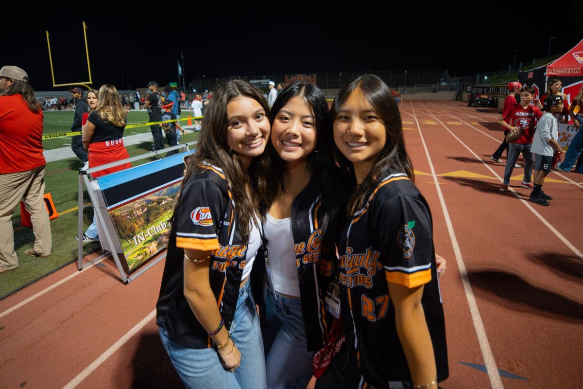 OCSS Staff members Kylie Wynn, Miranda Perdomo-Ballon and Emma Lin pose for a photo at Mission Viejo High School during a football game. 