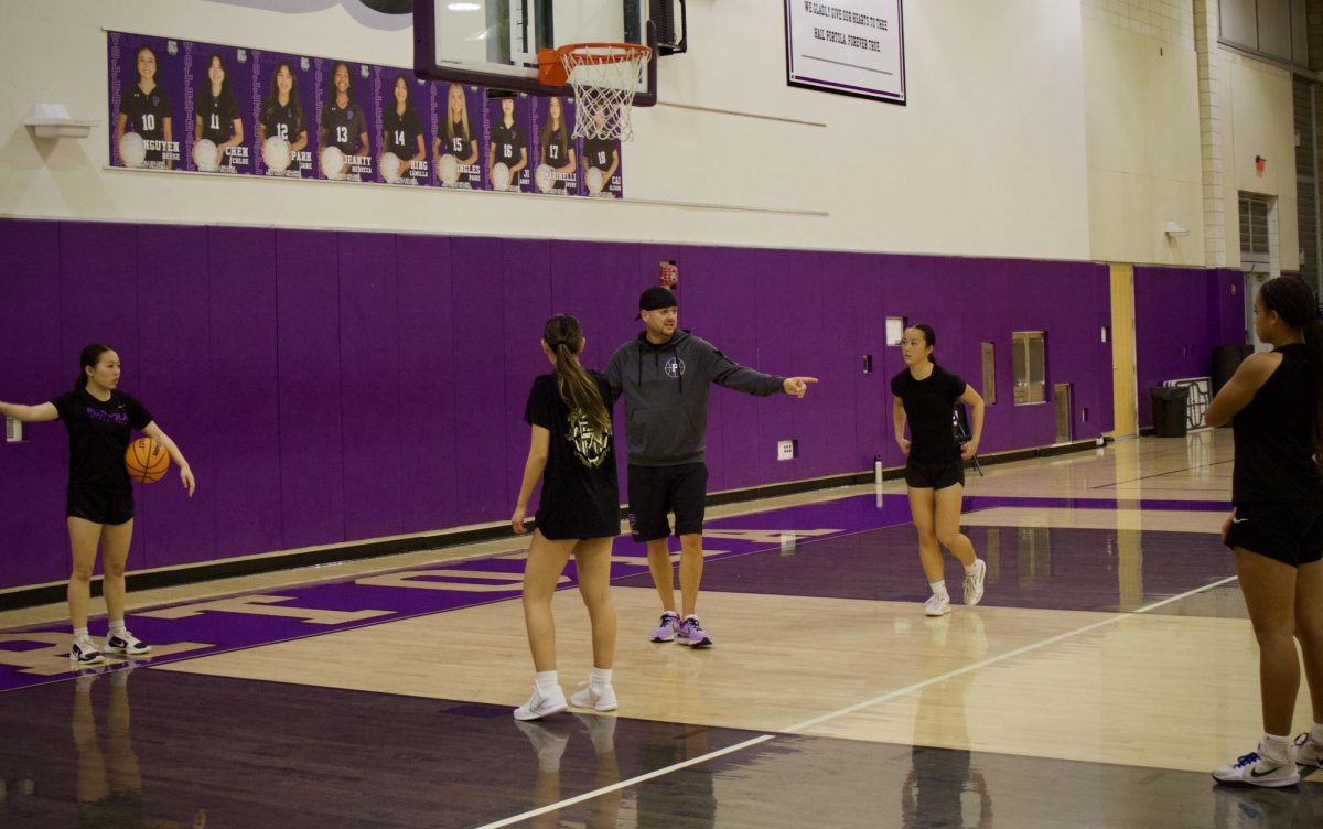 Girls basketball coach Brian Barham and point guard and senior Maddy Nguyen give pointers to the other team members after practicing shooting drills. 